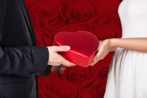 Gros plan mains de jeune couple avec boîte cadeau en forme de coeur rouge . — Photo