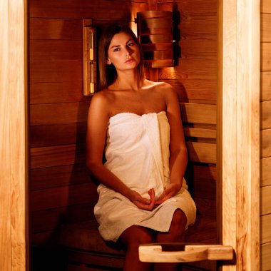 Beyaz havluya sarılmış güzel kadın ahşap sauna alır.