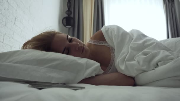 Sleepy woman turns alarm off while awakening in the morning. — Stock Video