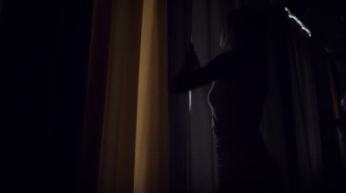 Genç kadın sabahın erken saatlerinde perdeleri açıyor.