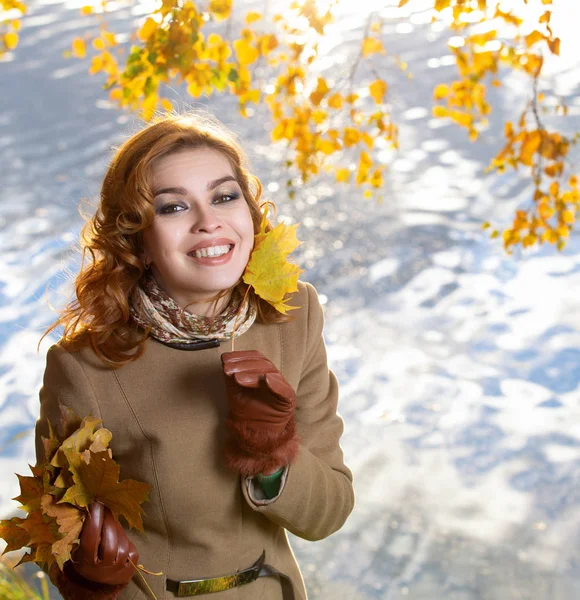 Young woman in the park and holds yellow autumn maple leaves.