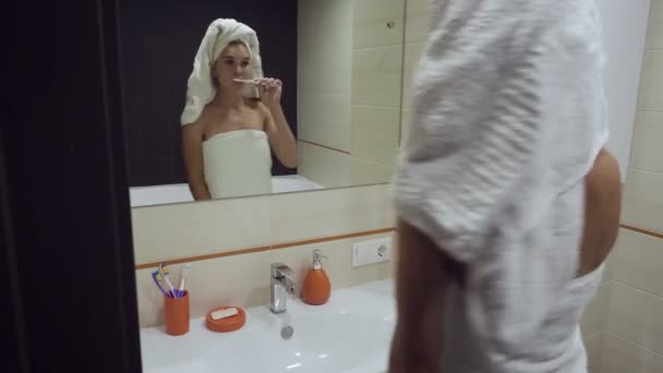 Όμορφη γυναίκα βουρτσίζει τα δόντια της και κοιτάζει στον καθρέφτη. — Αρχείο Βίντεο