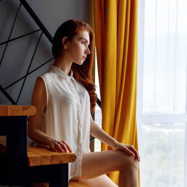 Loft dairede merdivenüzerinde oturan Kızıl saçlı kadın.