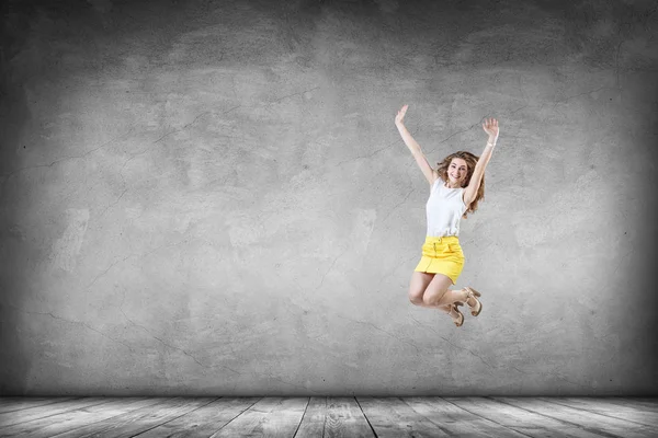 Happy young woman in yellow skirt jumps up. — Stock Photo, Image