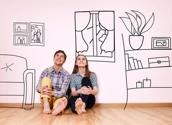 Happy couple sitting in their new flat among painted furniture on the wall. — Stock Photo, Image