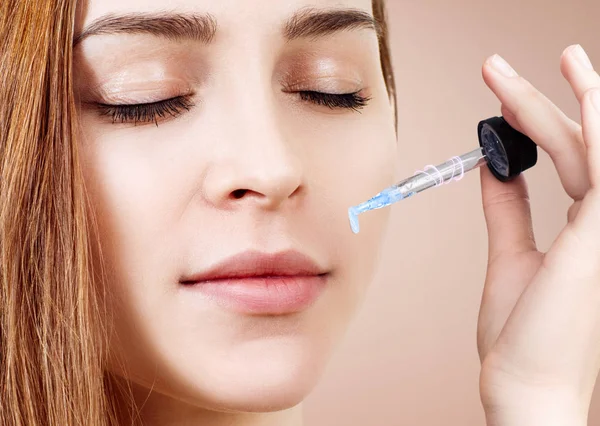 Mujer joven aplicando aceite cosmético en su cara . — Foto de Stock