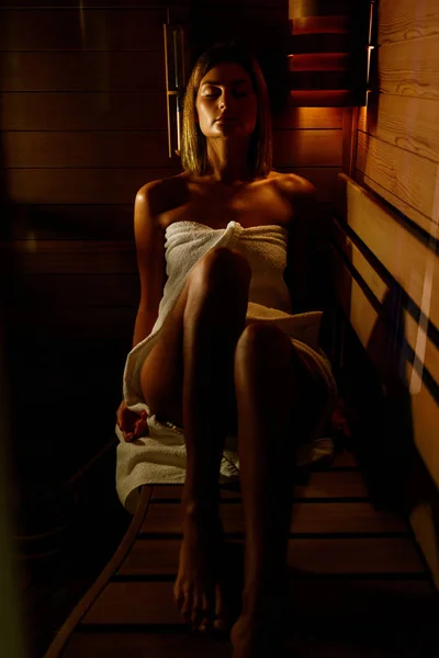 Beautiful woman wrapped in white towel takes a wooden sauna. — Stock Photo, Image