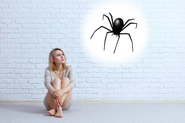 Młoda kobieta siedzi na podłodze i patrząc na Imaginary pająk. — Zdjęcie stockowe
