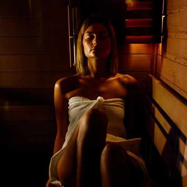 Femeia frumoasă înfășurată în prosop alb ia o saună din lemn . — Fotografie, imagine de stoc