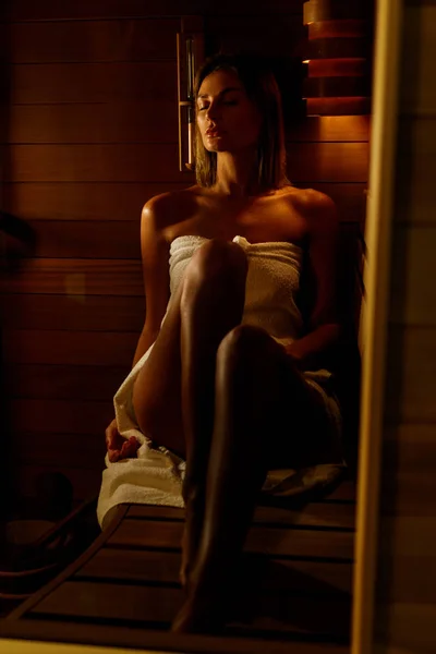 Beautiful woman wrapped in white towel takes a wooden sauna. — Stock Photo, Image