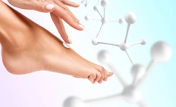 Hand toepassing cosmetische crème te voet in de buurt van witte moleculen. — Stockfoto