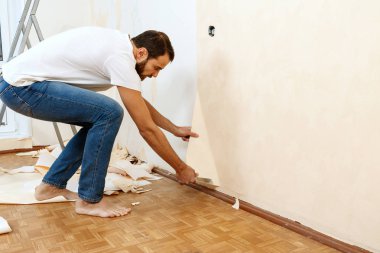 Eski duvar kağıdı kaldırma sürecinde bir kazıyıcı ile Adam.