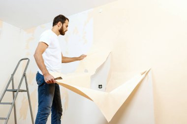 Eski duvar kağıdı kaldırma sürecinde bir kazıyıcı ile Adam.