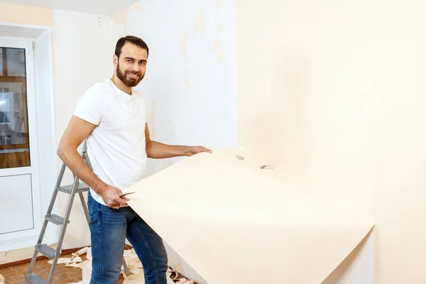 Hombre con un raspador en el proceso de eliminación de papel pintado viejo . —  Fotos de Stock