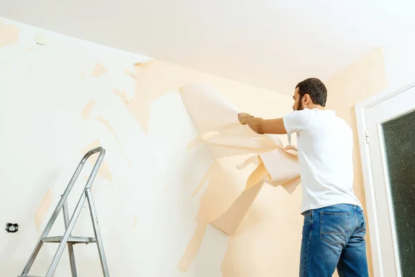 Hombre con un raspador en el proceso de eliminación de papel pintado viejo . —  Fotos de Stock