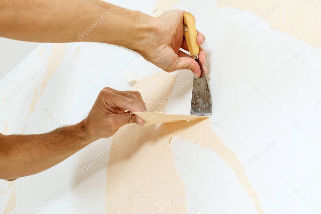 Close-up view on hands with a scraper in the process of removing wallpaper.