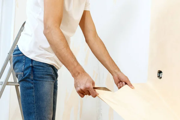 Hombre con un raspador en el proceso de eliminación de papel pintado viejo . —  Fotos de Stock