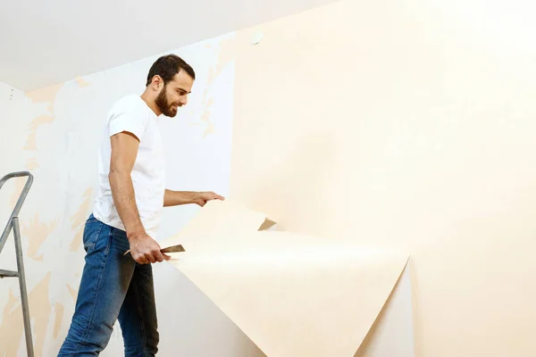 Hombre con un raspador en el proceso de eliminación de papel pintado viejo . —  Fotos de Stock