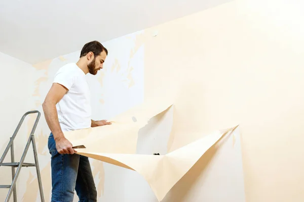 Hombre con un raspador en el proceso de eliminación de papel pintado viejo . —  Fotos de Stock