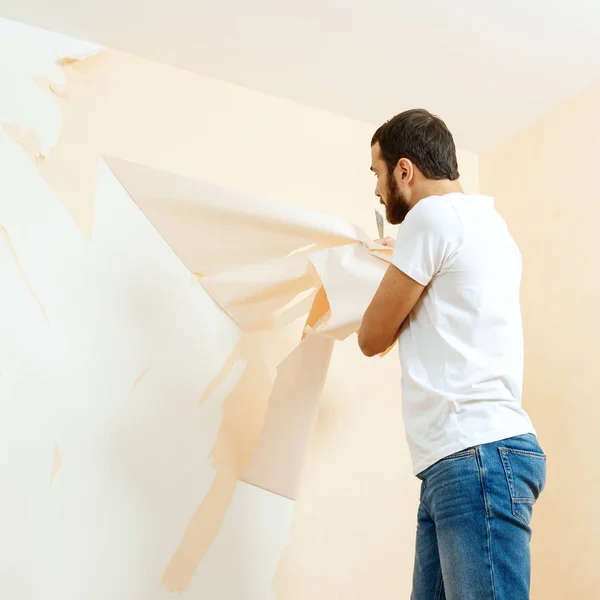 Hombre con un raspador en el proceso de eliminación de papel pintado viejo . —  Fotos de Stock