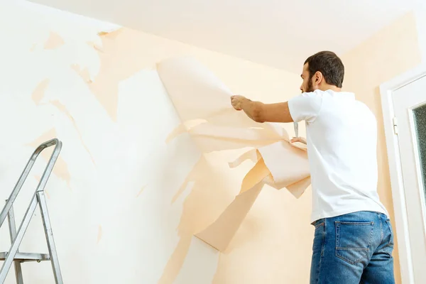 Hombre con un raspador en el proceso de eliminación de papel pintado viejo . —  Fotos de Stock