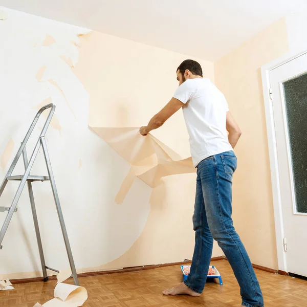 Hombre con un raspador en el proceso de eliminación de papel pintado viejo . —  Fotos de Stock