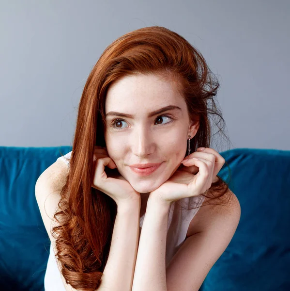 自宅の青いソファに座っている赤毛の女性. — ストック写真