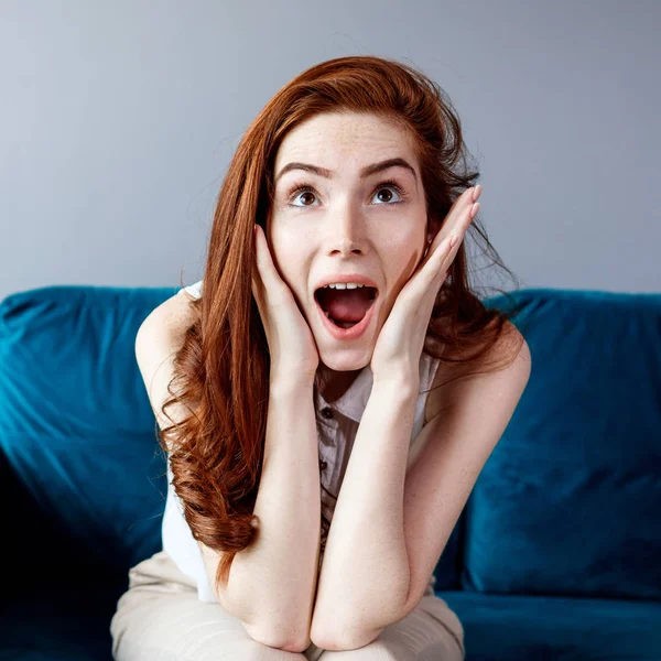 Redhead kvinna sitter på den blå soffan hemma. — Stockfoto