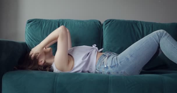 Young woman falling on sofa at home with a headache. — Stock Video