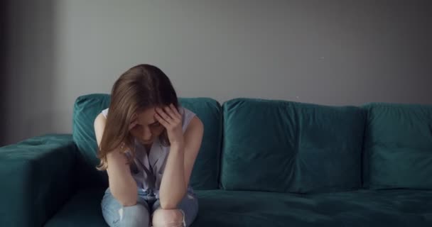 Young tired woman sits on sofa with a headache at home. — Stock Video