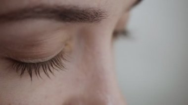 Kadın göz kırpıyor ve uzağa bakıyor.