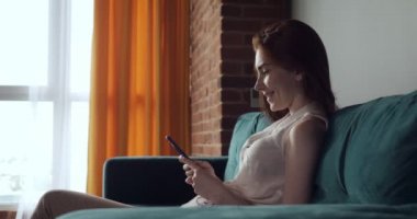 Genç kadın kanepede oturur ve akıllı telefon kullanarak.