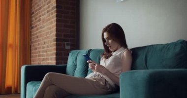 Genç kadın kanepede oturur ve akıllı telefon kullanarak.