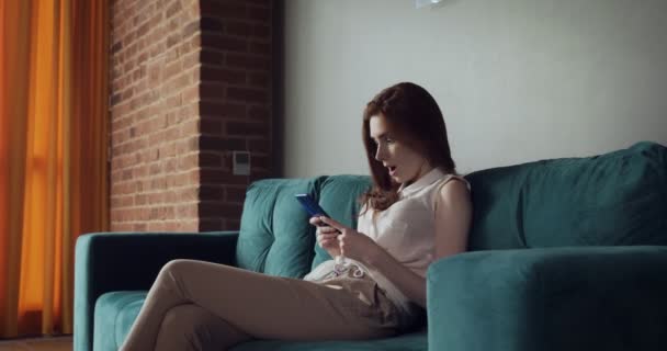 Mujer joven se sienta en el sofá y el uso de teléfonos inteligentes . — Vídeos de Stock