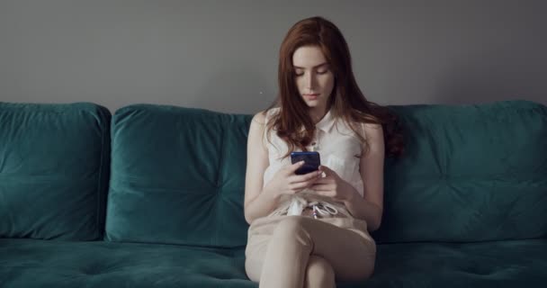 Young woman sits on the couch and using smartphone. — Stock Video