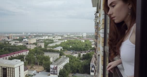 Mujer joven mirando la ciudad desde la ventana . — Vídeo de stock