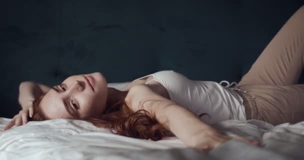 Молода руда жінка в домашньому одязі лежить на ліжку . — стокове відео