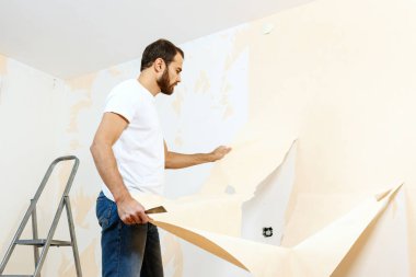 Eski duvar kağıdı kaldırma sürecinde bir kazıyıcı ile Adam.