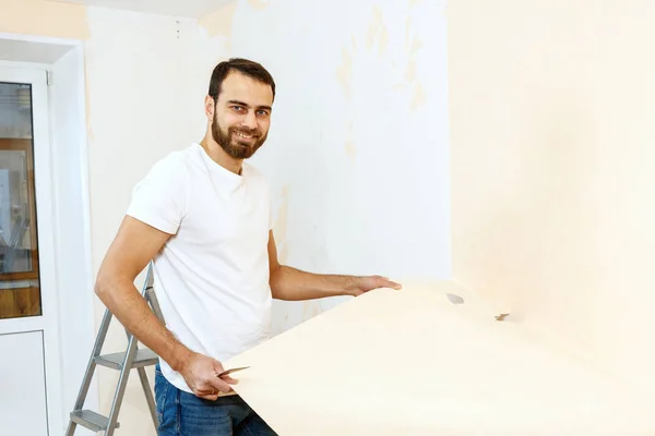 Hombre con un raspador en el proceso de eliminación de papel pintado viejo . —  Fotos de Stock