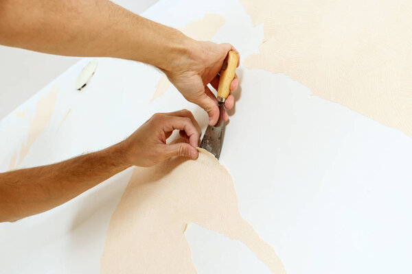 Close-up view on hands with a scraper in the process of removing wallpaper.