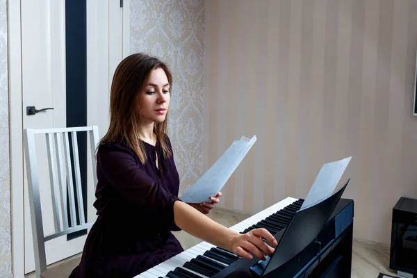 Mujer joven sentada y tocando en el piano electrónico — Foto de Stock