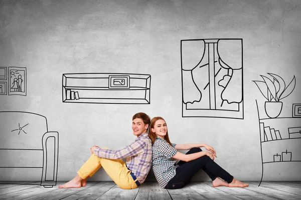 Happy couple sitting on the floor among painted furniture on the wall. — Stock Photo, Image