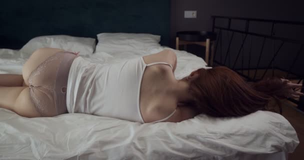 Achteraanzicht op jonge roodharige vrouw liggend op het bed. — Stockvideo