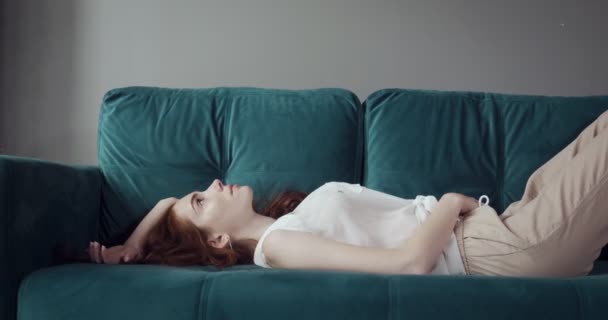 Κοκκινομάλλα κουρασμένη γυναίκα που πέφτουν στον καναπέ στο σπίτι με πονοκέφαλο. — Αρχείο Βίντεο