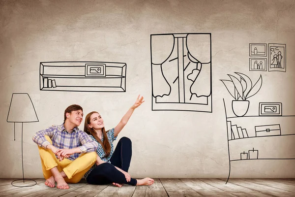 Happy couple sitting on the floor among painted furniture on the wall. — Stock Photo, Image