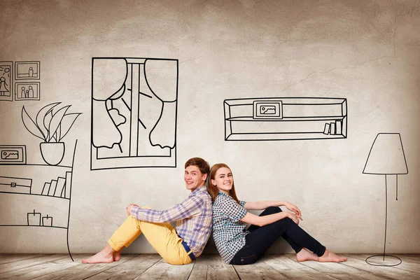 Счастливая пара, сидящая на полу среди раскрашенной мебели на стене . — стоковое фото
