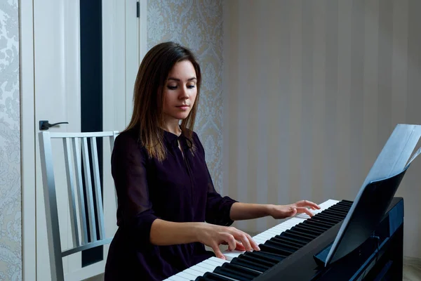 Mujer joven sentada y tocando en el piano electrónico — Foto de Stock