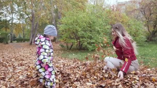 Madre y su pequeño bebé jugando con hojas en fallas en el parque de otoño . — Vídeos de Stock