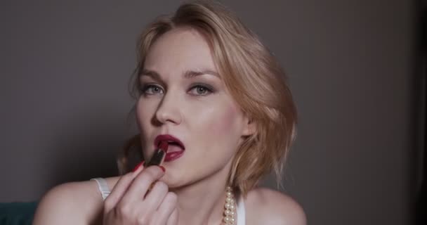Femme blonde mettant rouge à lèvres rouge sur les lèvres . — Video