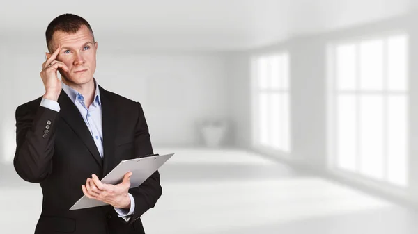 Thoughtful businessman posing in white office background. — Stock Photo, Image